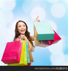 sale, gifts, holidays and people concept - smiling woman with colorful shopping bags over blue lights background