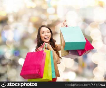 sale, gifts, holidays and people concept - smiling woman with colorful shopping bags over lights background