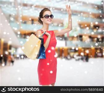 sale, gifts, holidays, gesture and people concept - smiling woman with colorful bags over shopping center background
