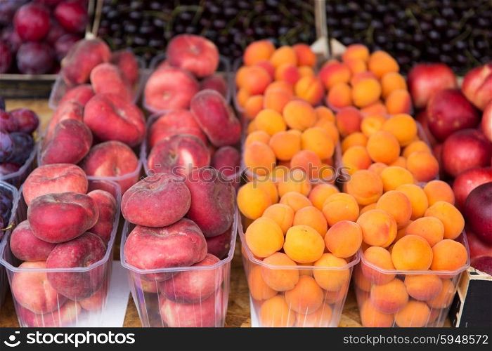 sale, harvest, food, fruits and agriculture concept - close up of flat peaches and apricots in plastic boxes at street market