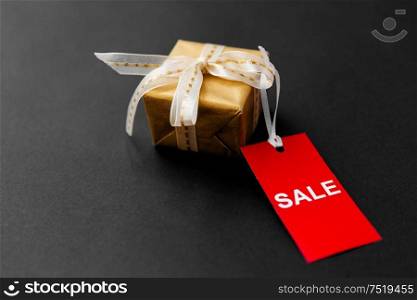 sale, holidays and christmas concept - small golden gift box and red discount tag on black background. small gift box and red sale tag with discount sign