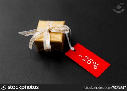 sale, holidays and christmas concept - small golden gift box and red discount tag with percent sign on black background. small gift box and red sale tag with discount sign
