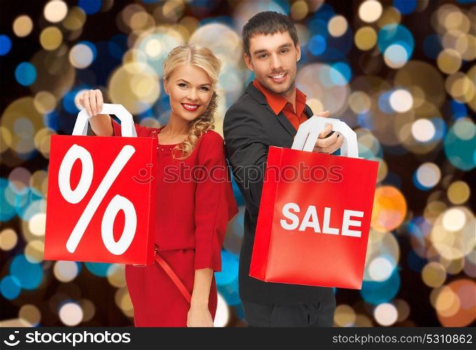 sale, holidays and people concept - happy couple with discount sign on shopping bags over christmas lights background. couple with sale and discount sign on shopping bag
