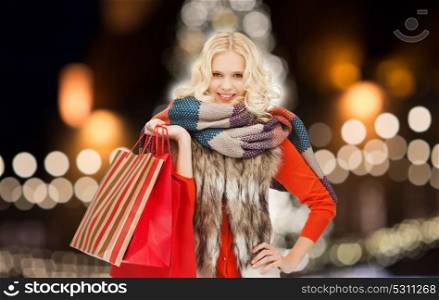 sale, holidays and people concept - happy teenage girl or young woman in winter clothes with shopping bags over christmas tree lights background. young woman in winter clothes with shopping bags