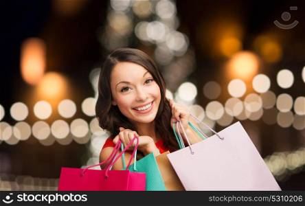 sale, holidays and people concept - smiling woman with shopping bags over christmas tree background . smiling woman with colorful shopping bags
