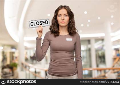 sale, lockdown and business concept - female shop assistant with closed sign and name tag over mall background. female shop assistant with closed sign