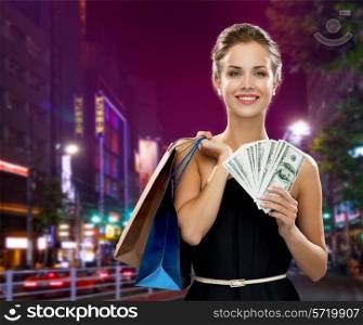 sale, money, people and holidays concept - smiling woman in evening dress with shopping bags and dollars over city background