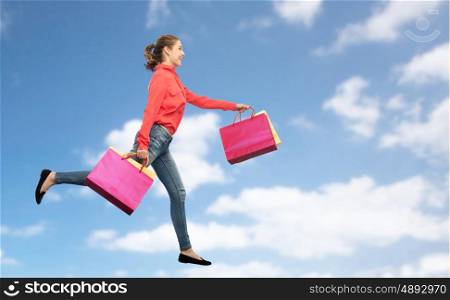 sale, motion and people concept - smiling young woman with shopping bags running in air over blue sky and clouds background