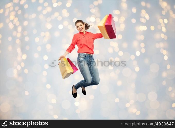 sale, motion and people concept - smiling young woman with shopping bags jumping in air over holidays lights background. smiling young woman with shopping bags jumping
