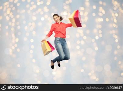 sale, motion and people concept - smiling young woman with shopping bags jumping in air over holidays lights background. smiling young woman with shopping bags jumping