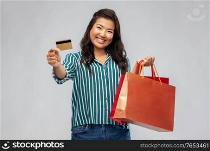 sale, outlet and consumerism concept - happy asian young woman with shopping bags and credit card over grey background. asian woman with shopping bags and credit card