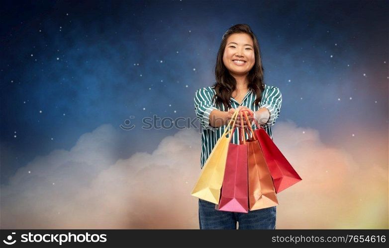 sale, outlet and consumerism concept - happy asian young woman with shopping bags over night sky and stars on background. happy asian woman with shopping bags on night sky