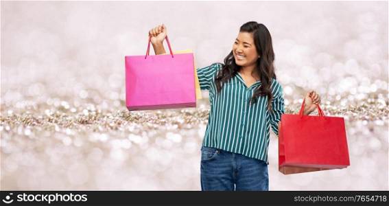 sale, outlet and consumerism concept - happy asian young woman with shopping bags over lights and glitter on background. happy asian woman with shopping bags
