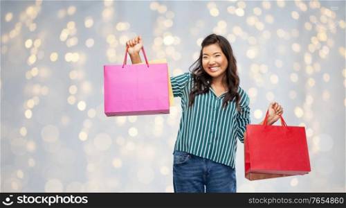 sale, outlet and consumerism concept - happy asian young woman with shopping bags over festive lights background. happy asian woman with shopping bags