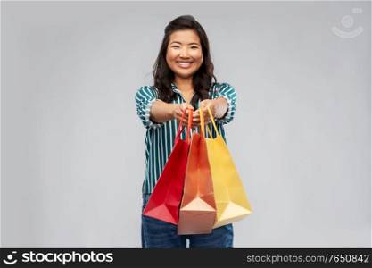 sale, outlet and consumerism concept - happy asian young woman with shopping bags over grey background. happy asian woman with shopping bags