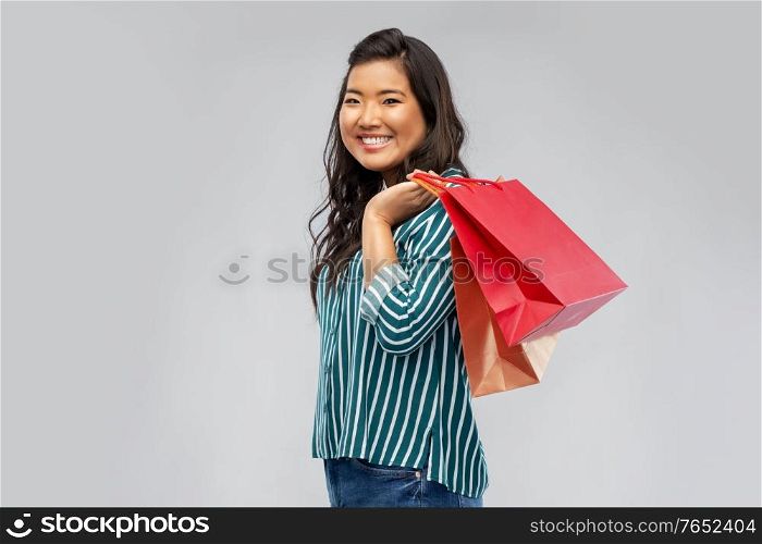 sale, outlet and consumerism concept - happy asian young woman with shopping bags over grey background. happy asian woman with shopping bags