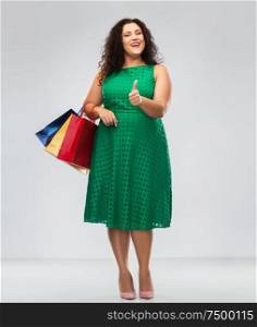 sale, outlet and consumerism concept - happy woman in green dress with shopping bags showing thumbs up over grey background. happy woman with shopping bags showing thumbs up