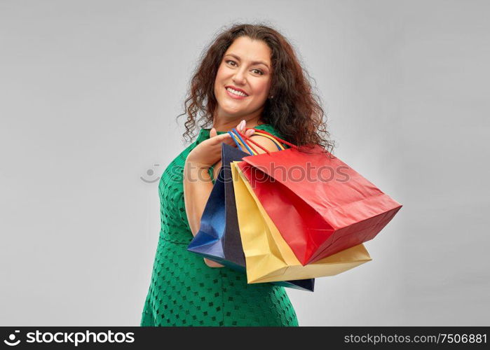 sale, outlet and consumerism concept - happy woman in green dress with shopping bags over grey background. happy woman in green dress with shopping bags