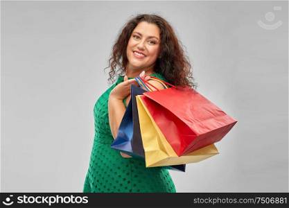 sale, outlet and consumerism concept - happy woman in green dress with shopping bags over grey background. happy woman in green dress with shopping bags