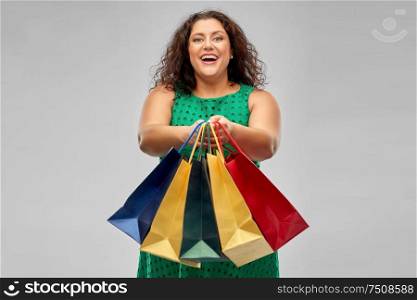 sale, outlet and consumerism concept - happy woman in green dress with shopping bags over grey background. happy woman in green dress with shopping bags