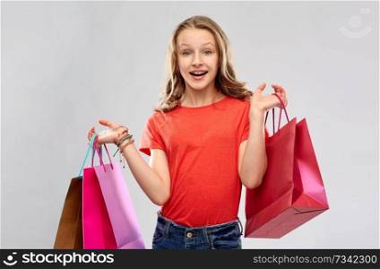 sale, outlet and people concept - smiling teenage girl in red t-shirt with shopping bags over grey background. smiling teenage girl with shopping bags