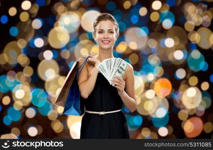 sale, people and holidays concept - smiling woman in dress with shopping bags and money over holidays lights background. smiling woman in dress with shopping bags