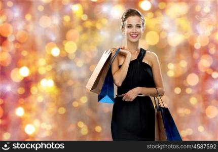 sale, people, christmas and holidays concept - smiling woman in dress with shopping bags over lights background