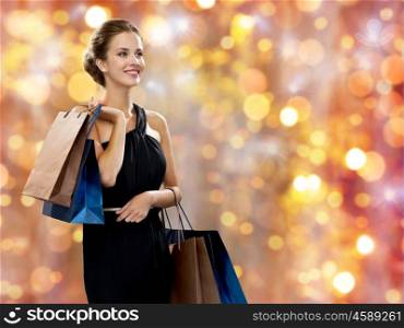 sale, people, christmas and holidays concept - smiling woman in dress with shopping bags over lights background