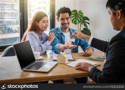 Sale representative offer the house key chain to Asian young couple after signed contact house purchase or rental on the working space table in new house,Moving and House Hunting concept