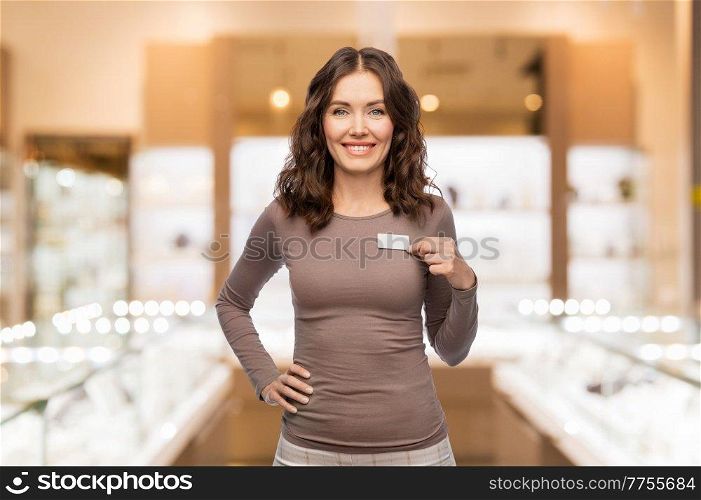 sale, shopping and business concept - happy female shop assistant showing her name tag over jewelry store background. female jewelry shop assistant showing her name tag
