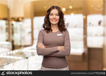 sale, shopping and business concept - happy female shop assistant with name tag and crossed arms over jewelry store background. happy female shop assistant at jewelry store