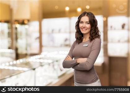 sale, shopping and business concept - happy female shop assistant with name tag and crossed arms over jewelry store background. happy female jewelry shop assistant with name tag