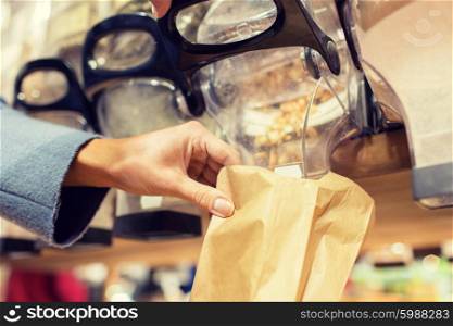 sale, shopping and eco food concept - close up of female hand pouring nuts to paper bag at grocery store