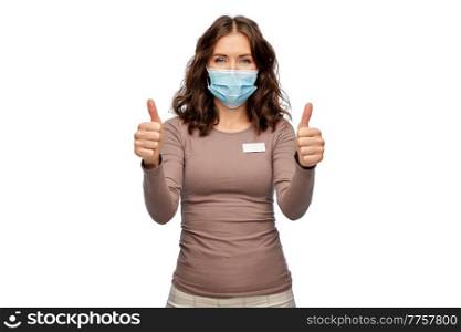 sale, shopping and pandemic concept - happy female shop assistant in medical mask with name tag showing thumbs up over white background. happy female shop assistant in medical mask