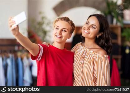 sale, shopping and technology concept - happy female friends taking selfie by smartphone at vintage clothing store. female friends taking selfie at clothing store