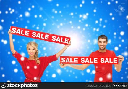 sale, shopping, christmas, holidays and people concept - smiling man and woman in red clothes with sale signs over blue snowy background