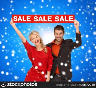 sale, shopping, christmas, holidays and people concept - smiling man and woman in red dress with red sale sign over blue snowing background