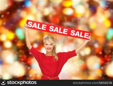 sale, shopping, christmas, holidays and people concept - smiling woman in red dress with red sale sign over lights background