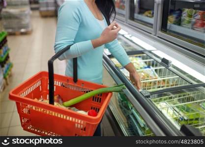 sale, shopping, consumerism and people concept - close up of woman with food basket at grocery store freezer