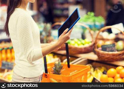 sale, shopping, consumerism and people concept - close up of young woman with food basket and tablet pc computer in market