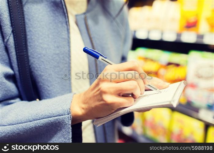 sale, shopping, consumerism and people concept - close up of young woman with pen taking notes to notebook in market
