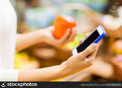 sale, shopping, consumerism and people concept - close up of young woman hands with smartphone and persimmon in market