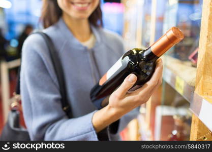 sale, shopping, consumerism and people concept - happy young woman choosing and buying wine in market or liquor store