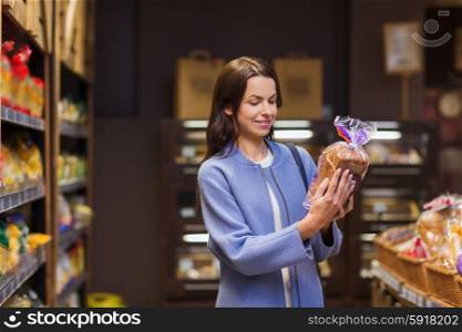 sale, shopping, consumerism and people concept - happy young woman choosing and reading label on bread in market
