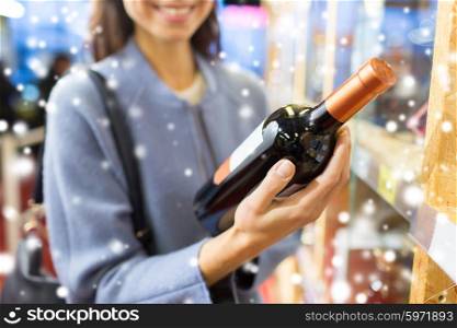 sale, shopping, consumerism and people concept - happy young woman choosing and buying wine in market or liquor store over snow effect