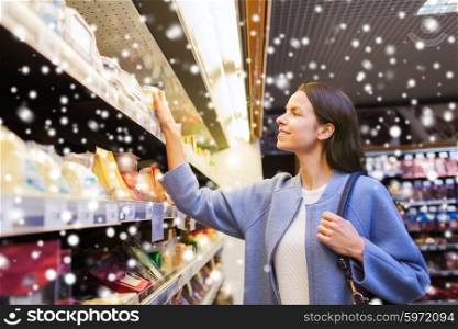 sale, shopping, consumerism and people concept - happy young woman choosing and buying food in grocery store over snow effect