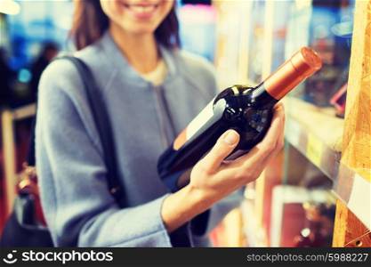 sale, shopping, consumerism and people concept - happy young woman choosing and buying wine in market or liquor store