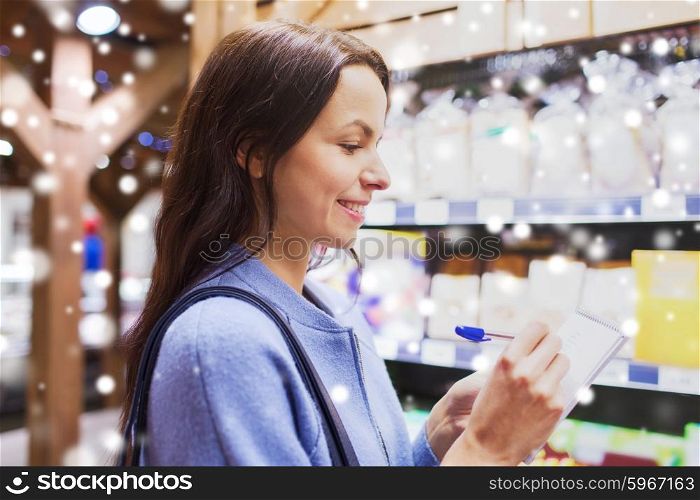 sale, shopping, consumerism and people concept - happy young woman taking notes to notebook in market over snow effect