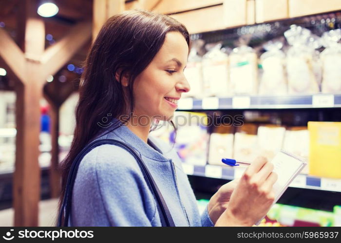 sale, shopping, consumerism and people concept - happy young woman taking notes to notebook in market