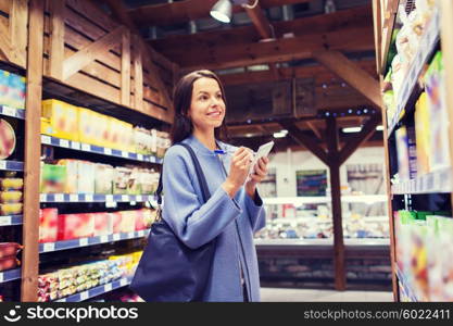 sale, shopping, consumerism and people concept - happy young woman taking notes to notebook in market